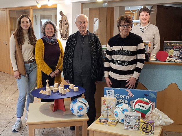 Fünf Personen mit gespendetem Spielzeug und Spielen, darunter Bälle, Holzbausteine und Brettspiele, auf Tischen.