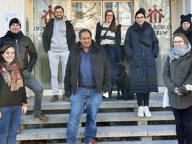 Sieben Erwachsene und ein schwarzer Hund posieren auf den Stufen des Don Bosco Zentrums.