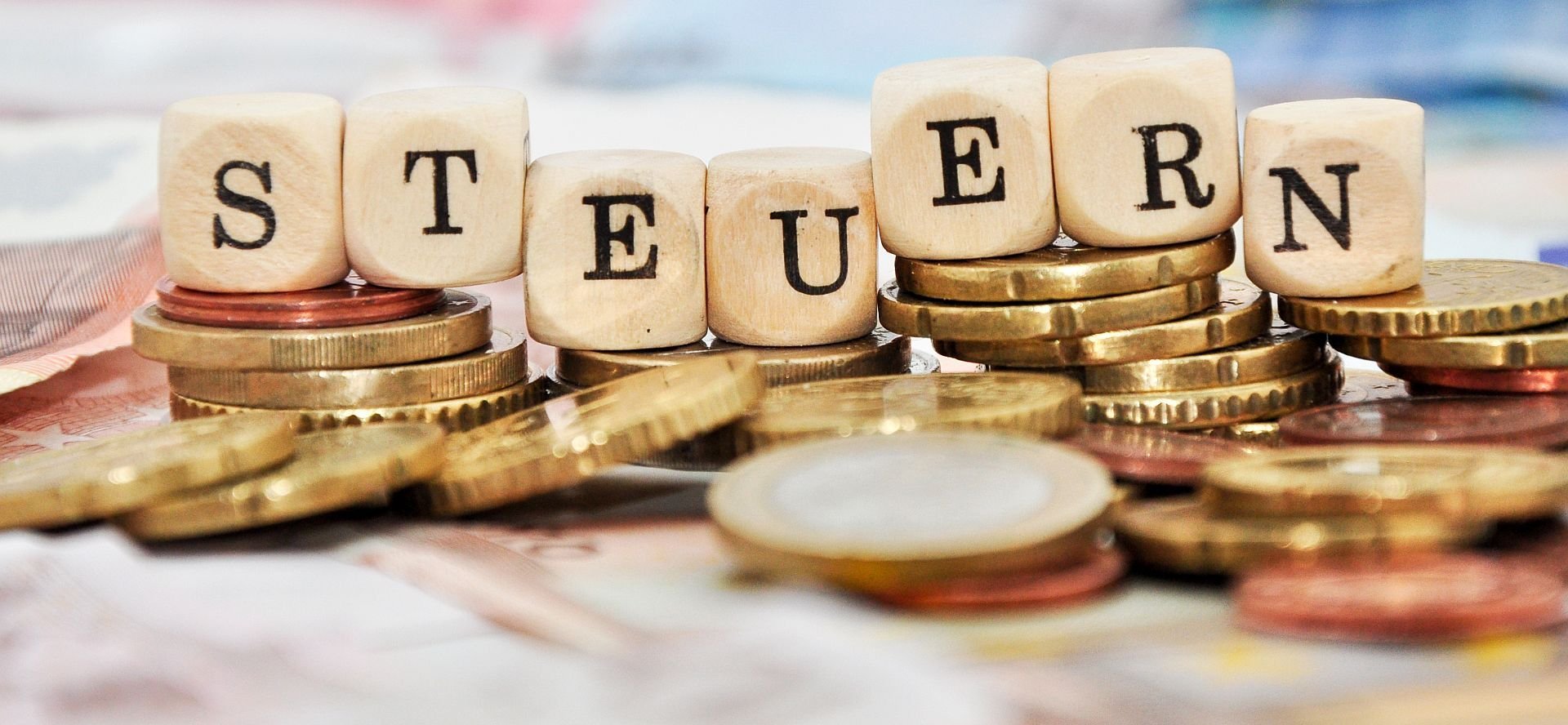 Ein Haufen Münzgeld und eine Reihe Holzwürfel, die das Wort "Steuern" buchstabieren.