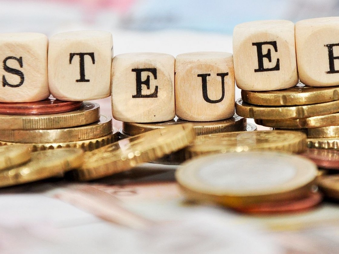 Ein Haufen Münzgeld und eine Reihe Holzwürfel, die das Wort "Steuern" buchstabieren.