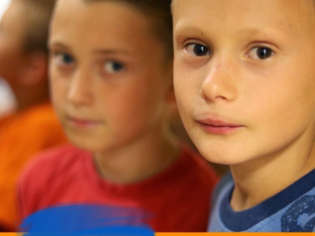 Zwei ernste Kinder, eines schaut in die Kamera, mit einem blau-gelben Pinselstrich und dem Text '#PRAYFORUKRAINE' unten.