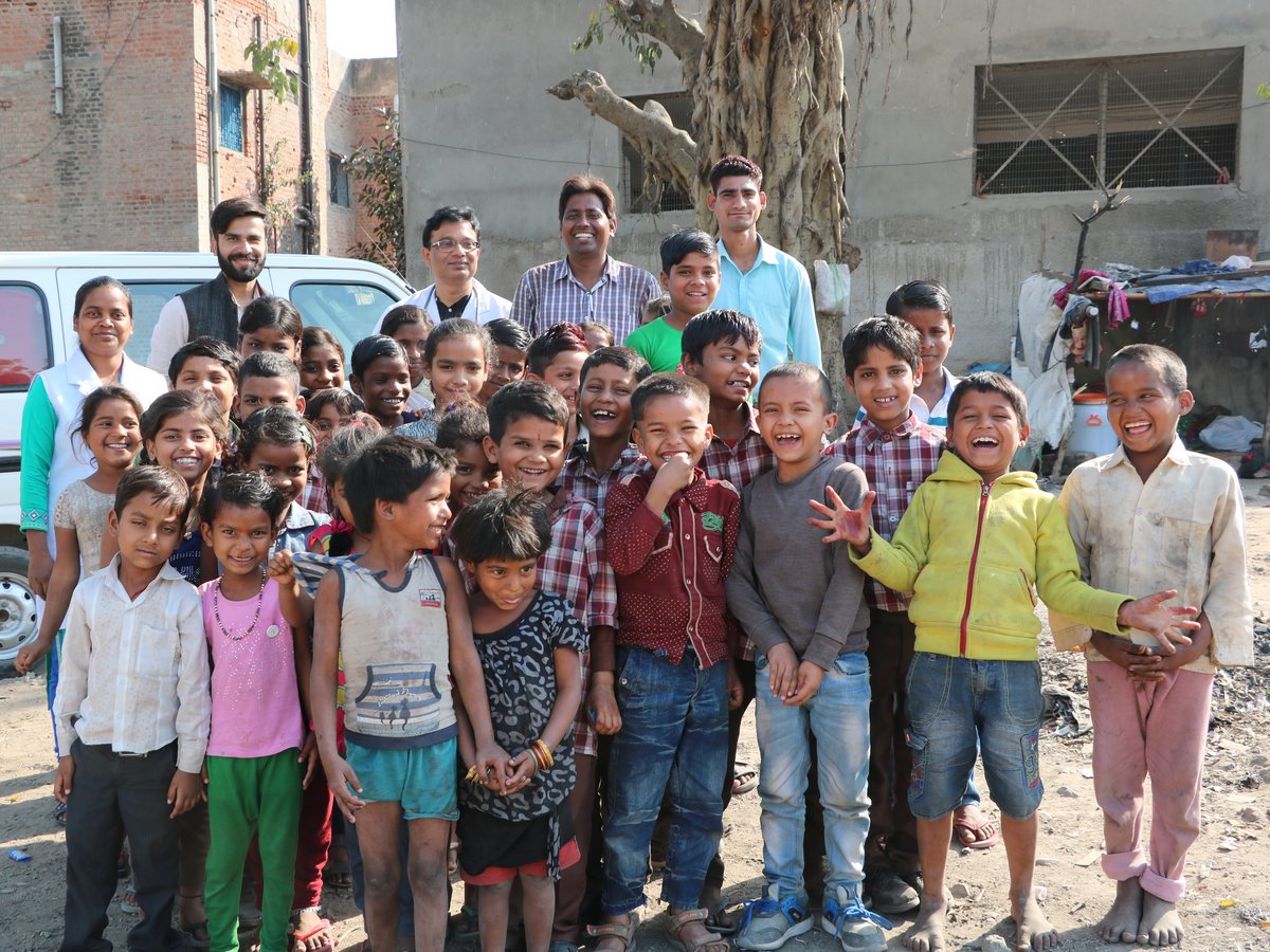 Eine vielfältige Gruppe lachender Kinder und Erwachsener, darunter medizinisches Personal, in einer sonnigen Gemeinschaft.