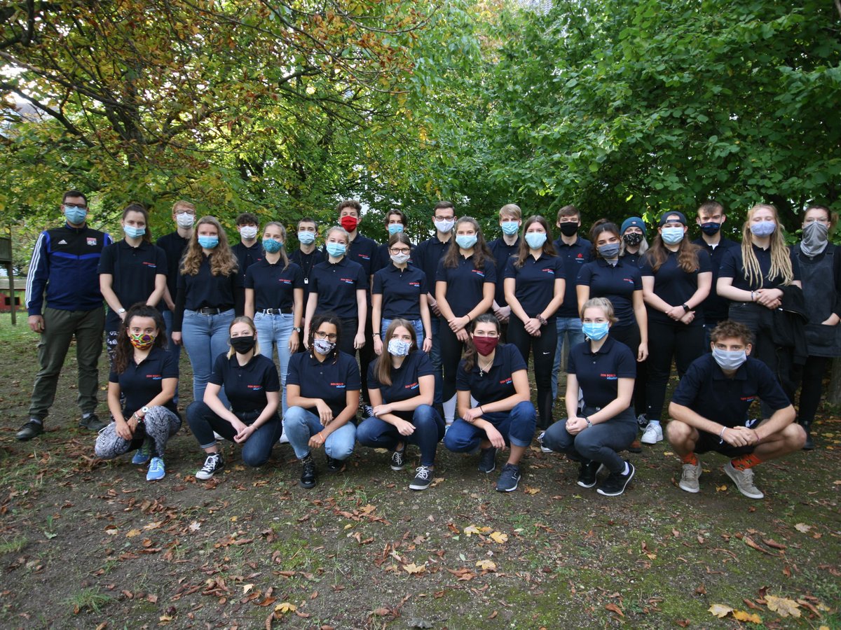 Junge Don Bosco Freiwillige tragen Masken für ein Gruppenfoto vor Herbstlaub und Bäumen.