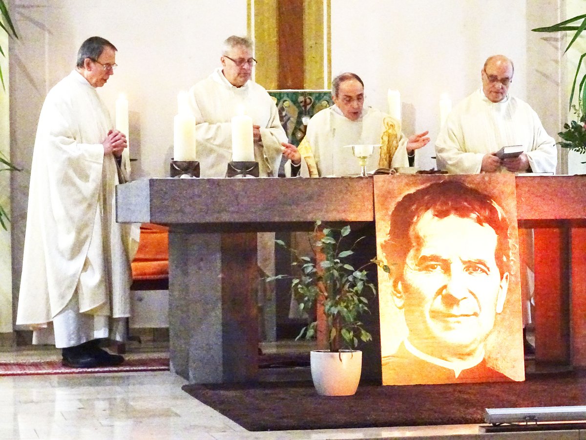 Vier Priester zelebrieren eine Messe in einer Kirche, mit einem großen Porträt des Heiligen Don Bosco neben dem Altar.