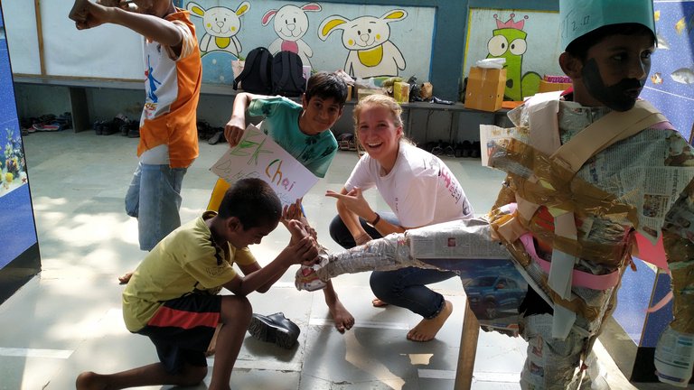 Kinder und eine Erwachsene basteln gemeinsam ein Zeitungskostüm. Ein Junge trägt eine Papierkrone, ein anderer zielt mit einem Spielbogen.