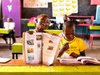Ein fröhliches afrikanisches Mädchen lacht mit einem Lehrbuch, neben einem Jungen, der in einem farbigen Klassenzimmer schreibt.