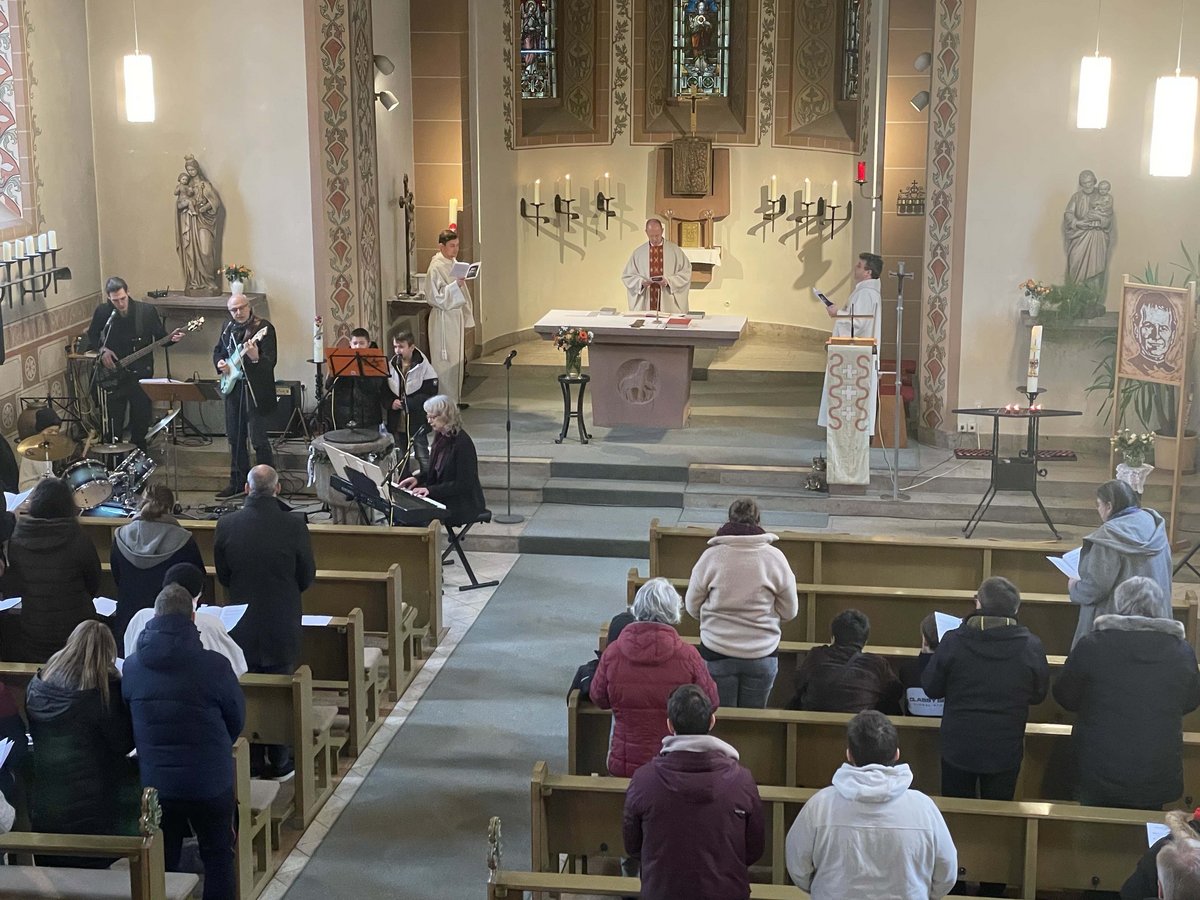 Ein moderner Gottesdienst in einer Kirche mit Priester am Altar, Live-Band und Gemeinde auf den Kirchenbänken.