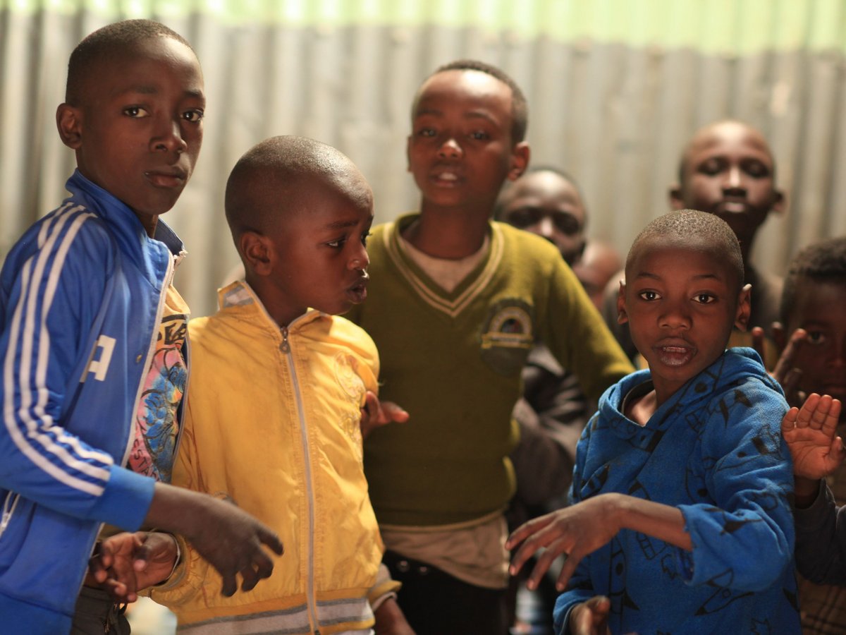 Junge afrikanische Kinder in bunten Jacken stehen eng beieinander in einem Raum, einige schauen direkt in die Kamera.