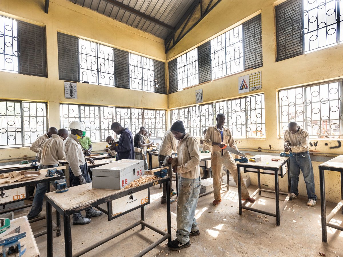 Junge Männer lernen Tischlerei in heller Werkstatt, arbeiten aktiv mit Handwerkzeugen an Holztischen zwischen Spänen.