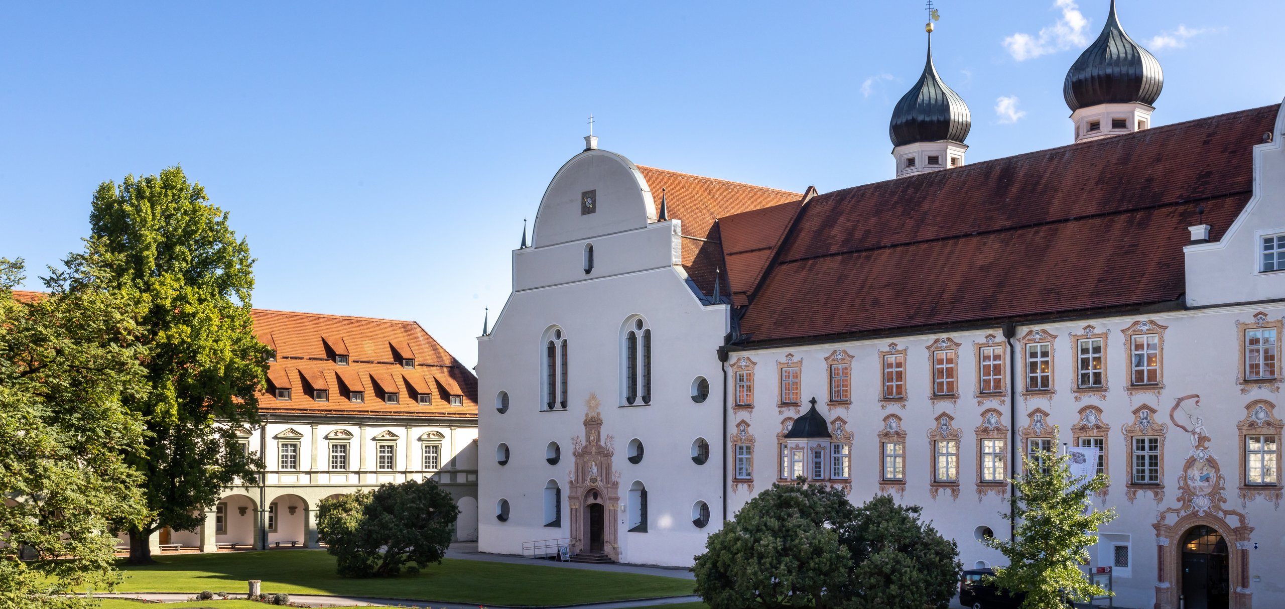 Ansicht Kloster seitlich mit Bäumen und Kirchtürmen im Hintergrund