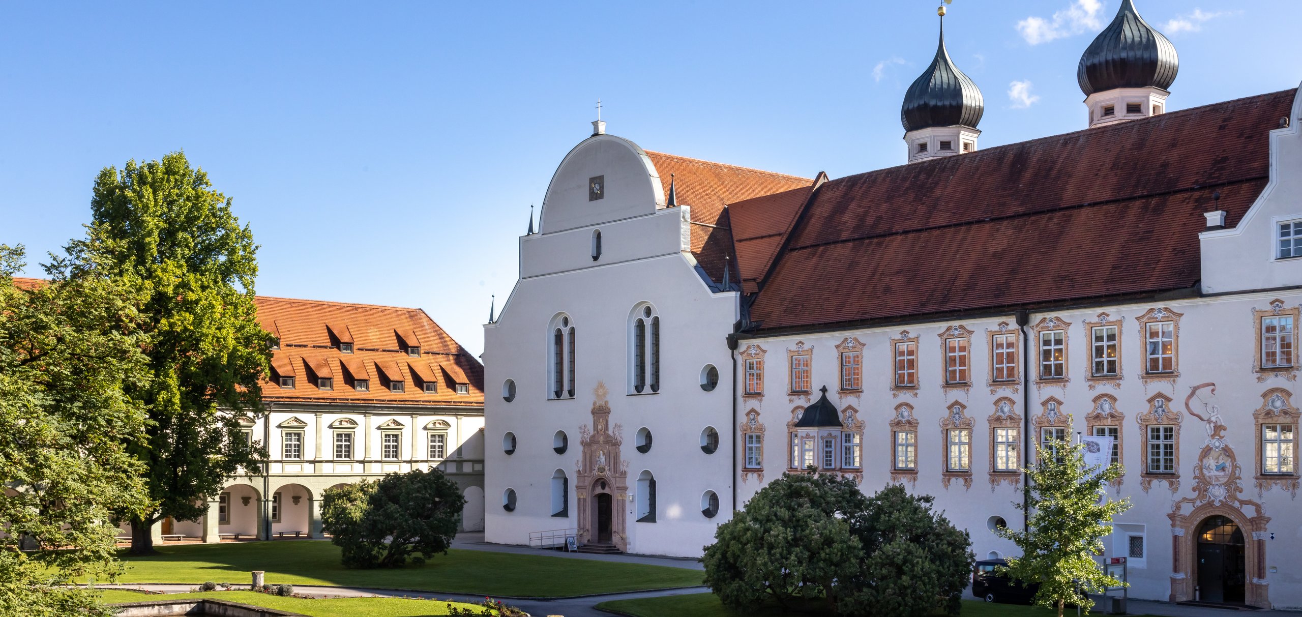 Ansicht Kloster seitlich mit Bäumen und Kirchtürmen im Hintergrund