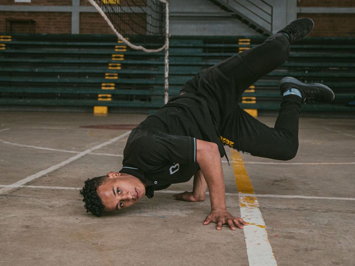 Junger Breakdancer in schwarzer Sportkleidung vollführt eine Freeze-Pose auf einem Betonplatz, balancierend auf Arm und Kopf.