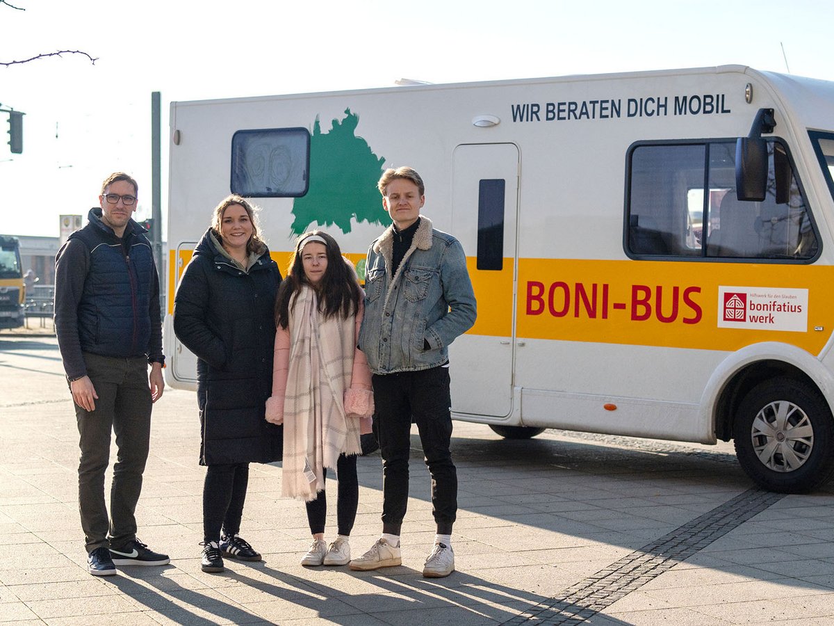 Vier Personen stehen vor dem weißen Boni-Bus des Bonifatiuswerks mit der Aufschrift 'Wir beraten dich mobil'.