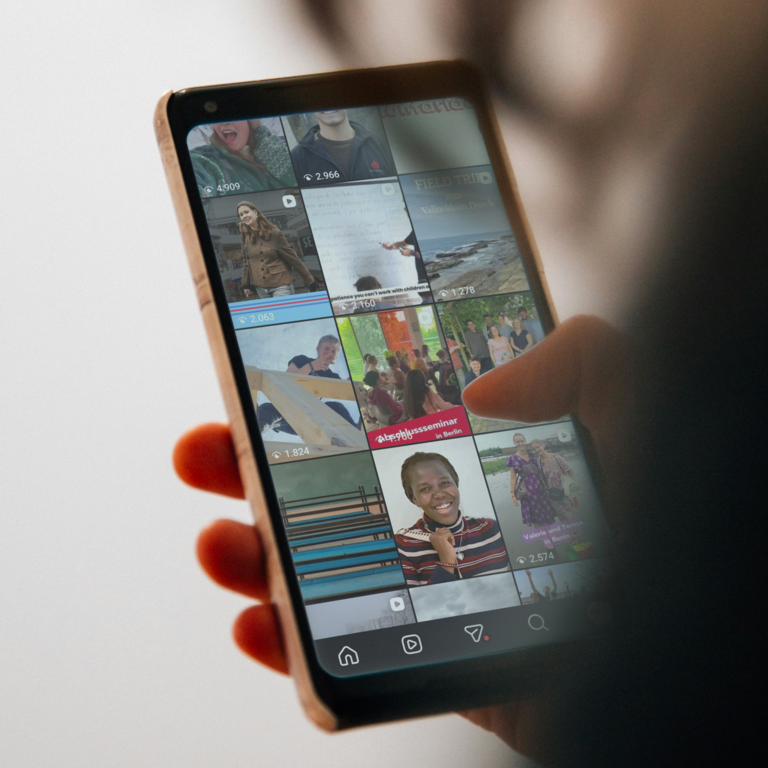 Eine Person hält ein Smartphone und scrollt durch einen Social-Media-Feed mit verschiedenen Bild- und Video-Miniaturen.