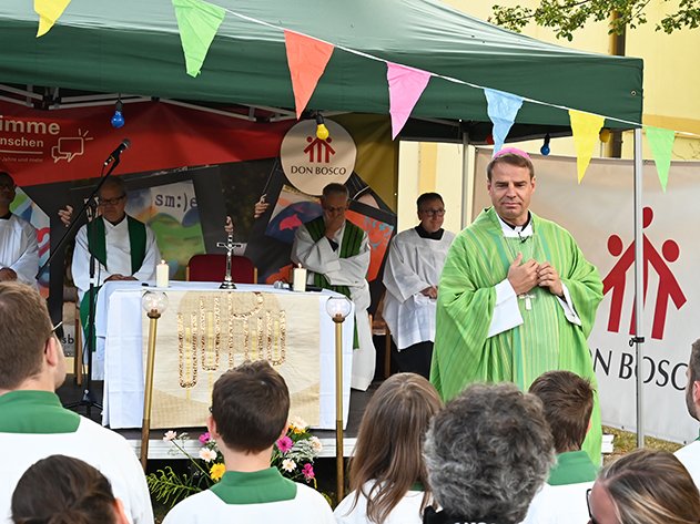 Bischof in grünem Gewand bei einem Don Bosco Gottesdienst im Freien mit Priestern und jungen Menschen.