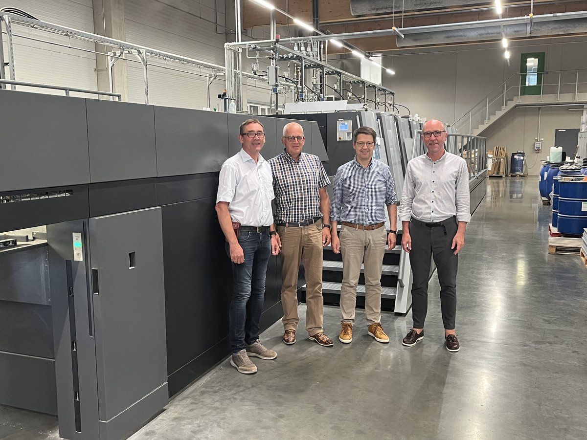 Vier Männer stehen vor einer großen, modernen Druckmaschine in einer hellen Produktionshalle.