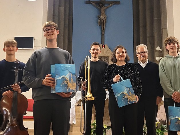 Gruppe von Musikern und einem älteren Mann, die nach einem Auftritt mit Geschenken in einer Kirche posieren.