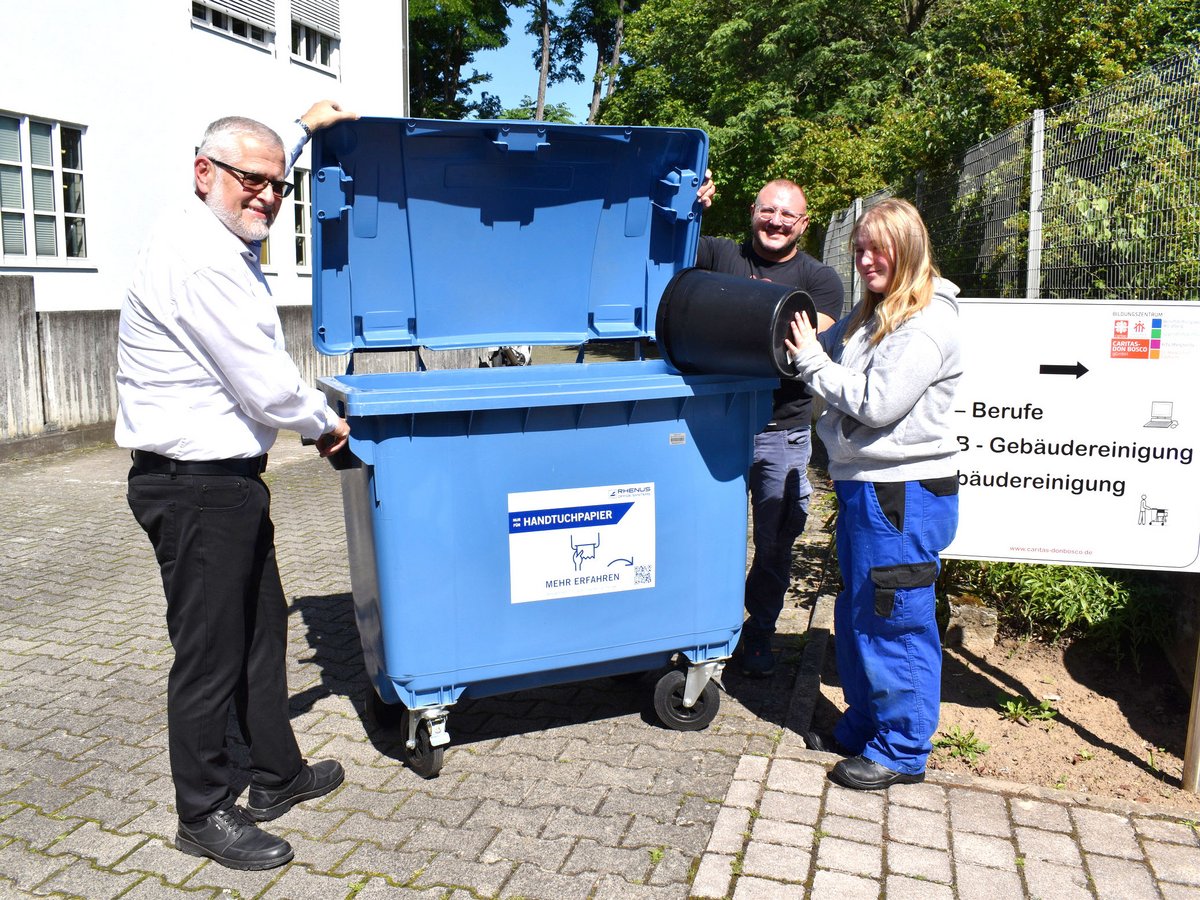 Drei Personen entsorgen Papiertücher in einer blauen Recyclingtonne für Handtuchpapier am Bildungszentrum.