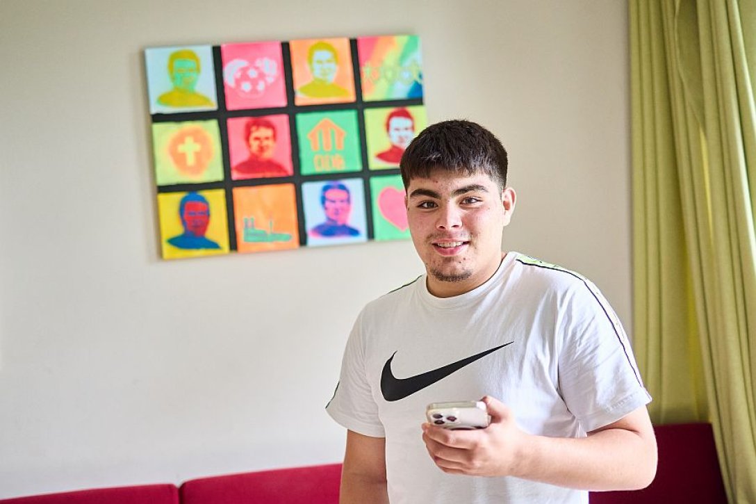 Ein Jugendlicher mit Mobiltelefon vor einem bunten Bild.