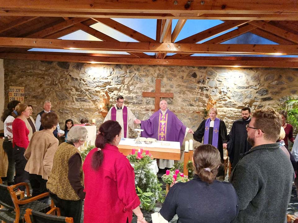 Eine vielfältige Gruppe bei einem Gottesdienst, Geistliche in Gewändern an einem Altar mit Adventskerzen.