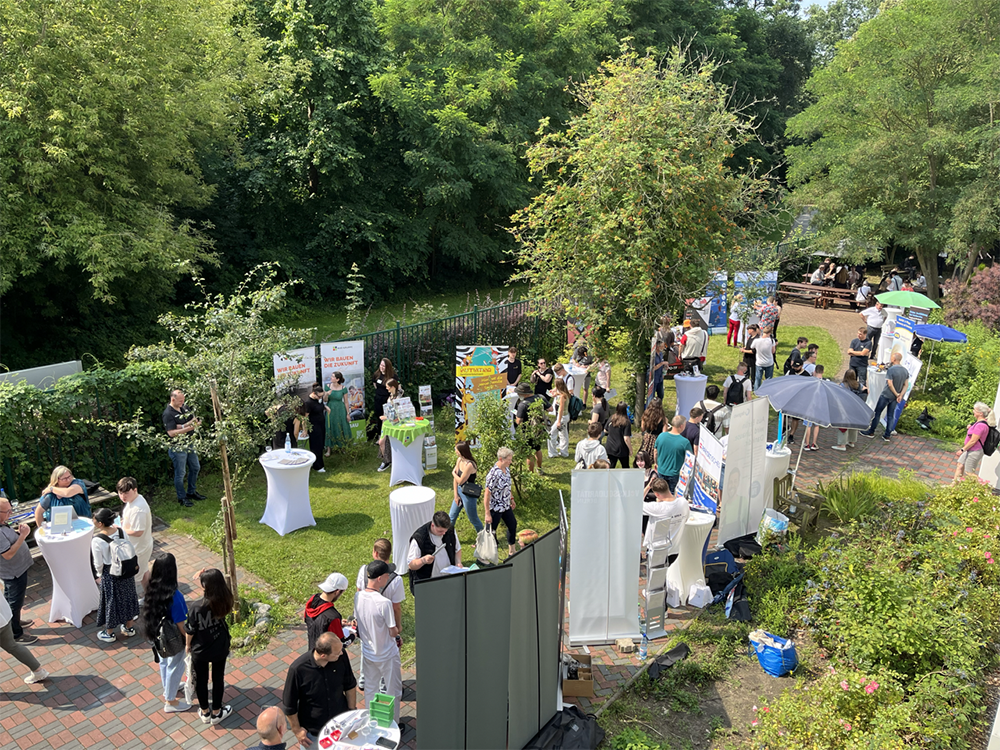Sonnige Veranstaltung im Freien mit vielen Menschen, die Stände durchstöbern und in einem grünen Park interagieren.