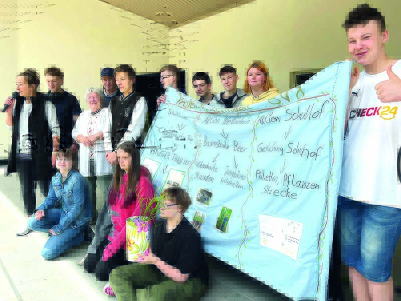 Gruppe von Schülern und Erwachsenen präsentiert ein Banner zum Thema 'Aktion Schulhof' mit Plänen für Pflanzen und Sitzecken.
