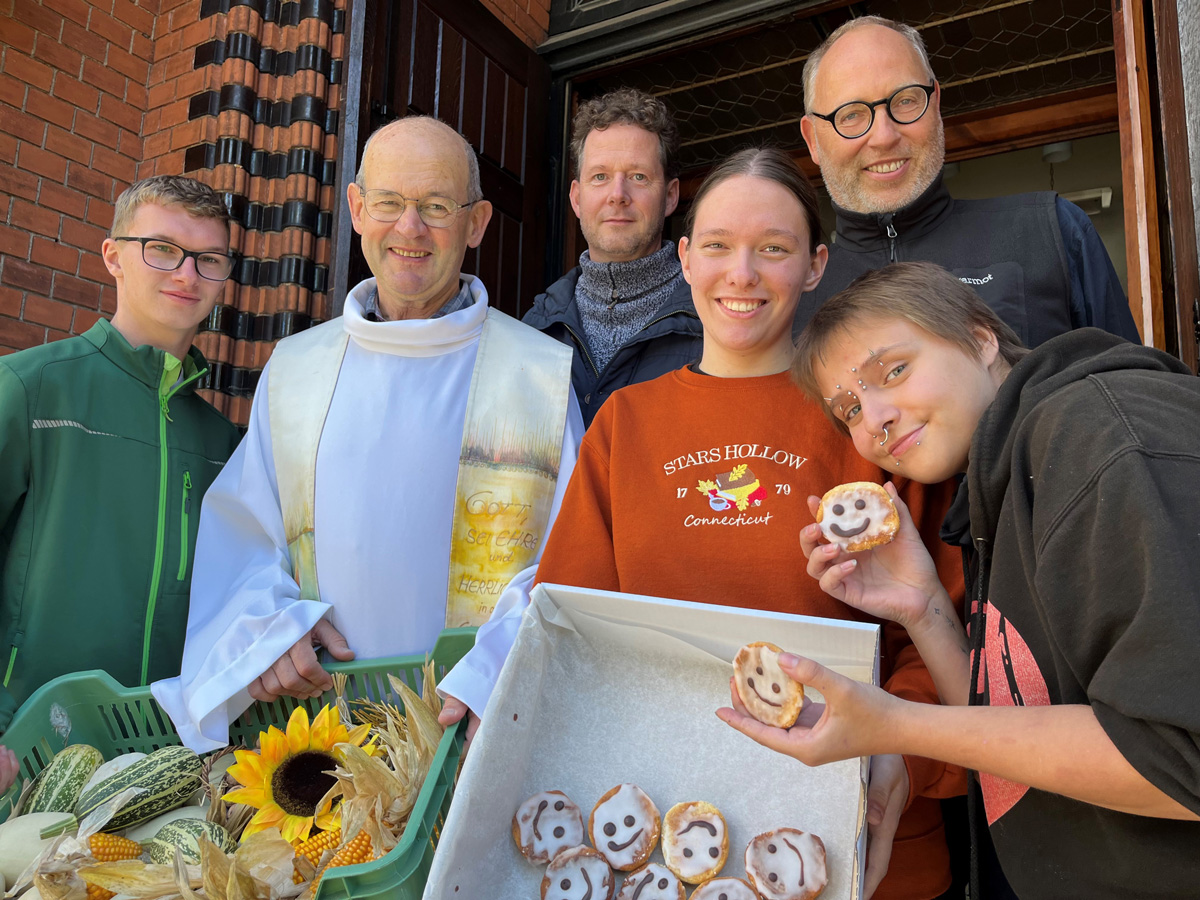 Lachende Gruppe mit Priester, der eine Kiste mit Smiley-Keksen und einen Korb mit Herbstdekorationen hält.
