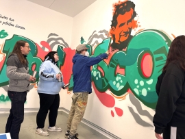 Drei junge Menschen sprühen ein Graffiti.