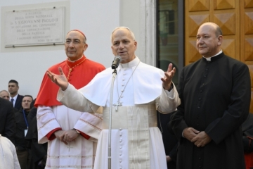 Links ein Priester mit weißem Gewand und rotem Umhang, in der Mitte der Papst in weißem Gewand und silberner Bauchbinde, rechts ein Priester in schwarzem Gweand.