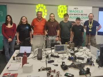 Schülerinnen, Schüler und Lehrer stehen vor einem Tisch mit Elektrogeräten