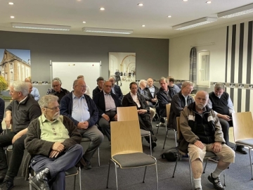 Die am Provinzgemeinschaftstag teilnehmenden Pater sitzen auf Stühlen im Konferenzraum.