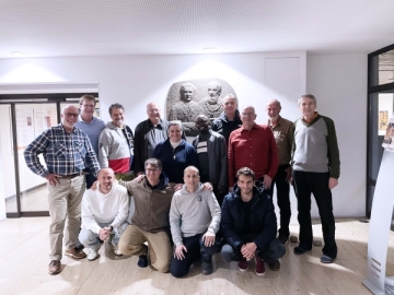 Vierzehn Männer unterschiedlicher Hautfarbe stehen vor einer Don Bosco Statue