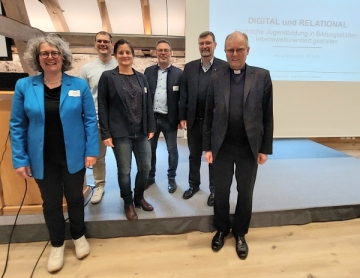 Sechs Frauen und Männer stehen auf einem Podium vor einer Leinwand.