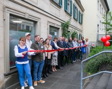eine Reihe von Menschen steht vor einem Gebäude und hält ein rotes Band in der Hand.