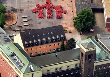 Luftaufnahme eines Schulhofs in Essen, auf dem zahlreiche Personen ein menschliches Symbol in Form einer Figurengruppe darstellen