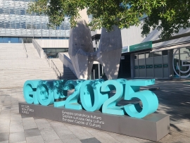 Vor einem Baum steht eine Skulptur in türkis: GO 2025