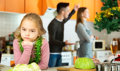 Ein Mädchen blickt in die Kamera, während im Hintergrund die Eltern streiten.