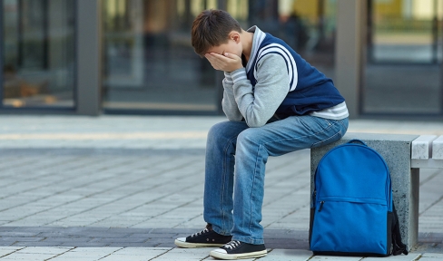 Junge sitzt auf einer Bank und hat die Hände vors Gesicht geschlagen