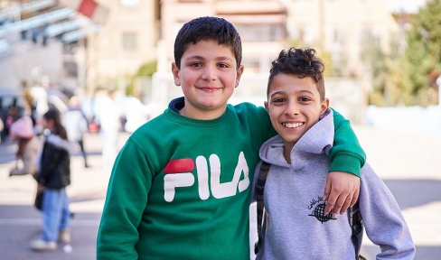 zwei Jungen lachen mit umeinander gelegten Armen in die Kamera