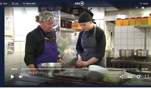 Zwei Frauen stehen mit Schürze und Kopftuch in einer Profiküche und schneiden Lebensmittel.