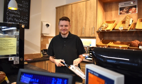 Christian Friebel steht hinter der Bäckereitheke und befüllt eine Tüte mit Ware.