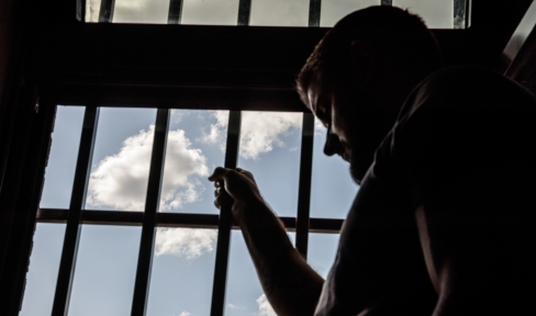 Ein junger Mann steht vor einem vergitterten Fenster.