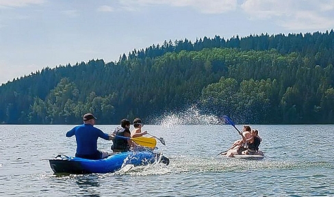 Jugendliche und Betreuer in Booten auf See vor Wald 