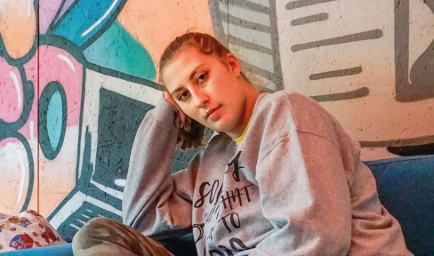 Eine junge Frau sitzt auf einem blauen Sofa und blickt auf ihren Arm gelehnt in die Kamera