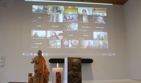 Kerze, Karte und Don Bosco Figur stehen auf dem Tisch – dahinter ist der Bildschirm der Zoom-Konferenz zu sehen.