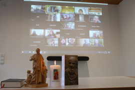 Kerze, Karte und Don Bosco Figur stehen auf dem Tisch – dahinter ist der Bildschirm der Zoom-Konferenz zu sehen.